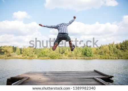 Image from back of jumping man on wooden bridge by river