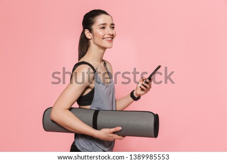 Image of amazing beautiful young pretty fitness woman using mobile phone holding rug isolated over pink wall background.