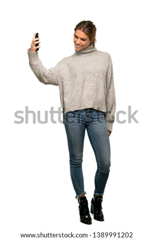 A full-length shot of a Blonde woman with turtleneck making a selfie over isolated white background