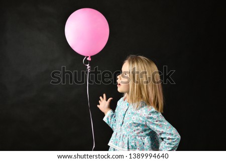 The girl on a black background blows a balloon.