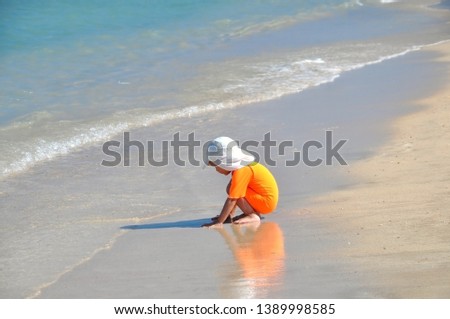 A little girl in an orange swimsuit sits on the beach on a sunny day. Child on the background of the sea. The girl in orange relaxes looking at the sea. Water is the source of life. Healthy lifestyle.