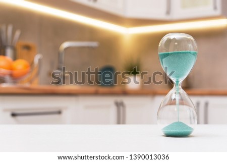 Closeup of hourglass on a white wooden table with defocus kitchen on background. Concept of time to cook.