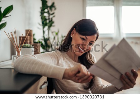 Smiling woman looking at received mail at home, close-up. Royalty-Free Stock Photo #1390020731