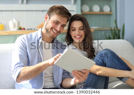 Young couple watching media content online in a tablet sitting on a sofa in the living room. Royalty-Free Stock Photo #1390032446