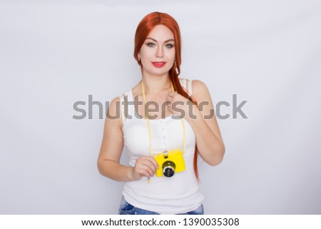 Happy pretty redhead woman wearing white tshirt making photo and looking at yellow camera over white background