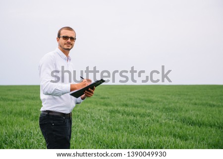 young handsome agronomist, agriculture engineer standing in green wheat field with tablet in hands in early summer. Agribusiness concept.