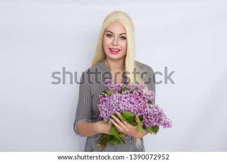 Picture of pleasured blonde woman in shirt takes bouquet of lilac flowers over white background