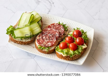 Fresh sandwiches with sausage, cheese, bacon, tomatoes, lettuce, cucumbers on a light background. Horizontal orientation
