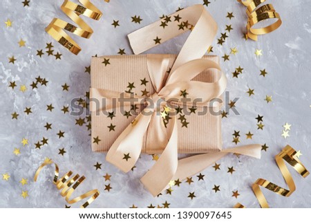 Gift box wrapped in kraft paper with golden bow and confetti in shape star, close up