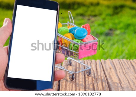 Macarons in small metal shopping cart and smartphone on green background
