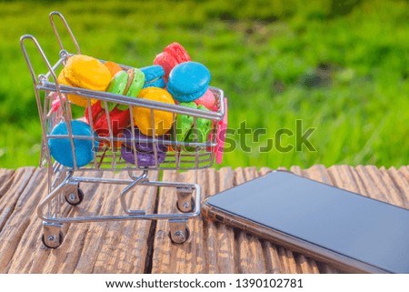 Macarons in small metal shopping cart and smartphone on green background