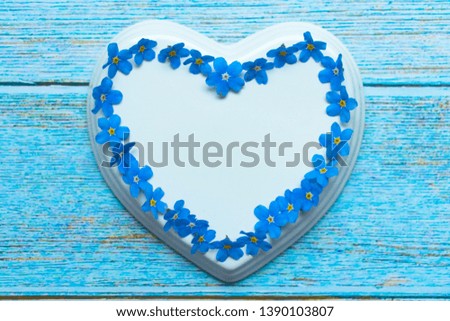 White porcelain heart and blue flowers laid out in the shape of a heart on a blue wooden background 