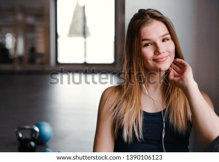 A young girl or woman with earphones and smartphone in a gym.