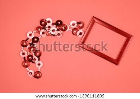 Empty picture frame with trail of wooden necklace on coral colored background