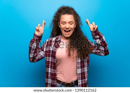 Teenager girl over blue wall with fingers crossing and wishing the best