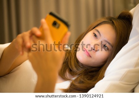 Sleepy woman lying on bed and using smart phone at late night. Conceptual of social media addiction.