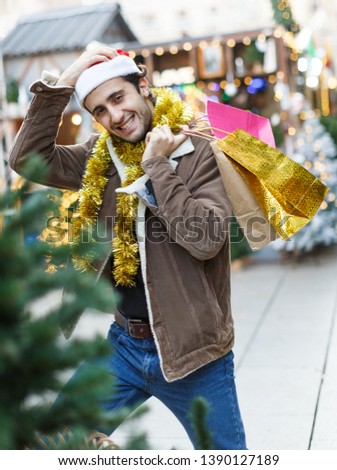 Portrait of young man in Christmas  hat  with purchases  at Christmas market