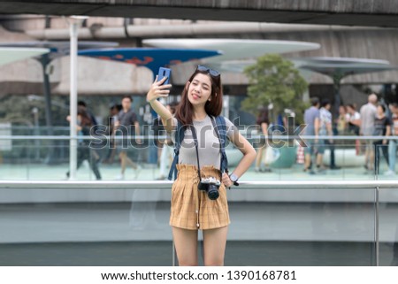 Attractive young Asian woman taking photo or selfie outdoors in urban