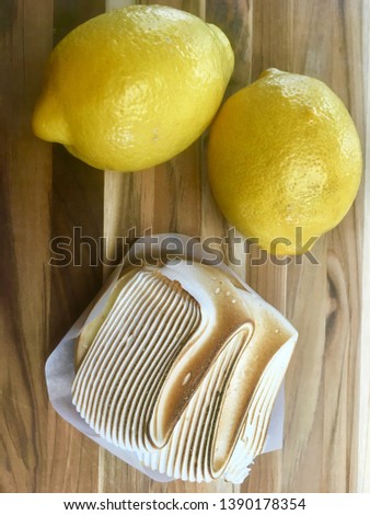 Lemon Meringue Tart and Lemons.  A Lucious lemon meringue Tart sits on a teak wooden board with two tart lemons.