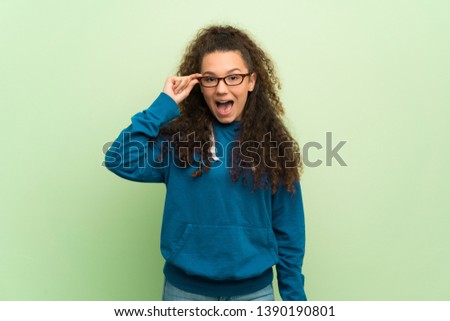 Teenager girl over green wall with glasses and surprised