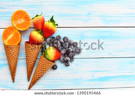 Cone ice cream with fresh fruit consist cut tangerine, strawberry, frozen blueberry on blue wooden plank background with copy space, fruity for flavor ice cream, delicious dessert for summer, minimal 