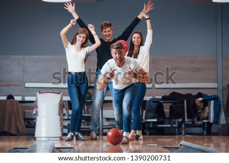 This is win. Young cheerful friends have fun in bowling club at their weekends.