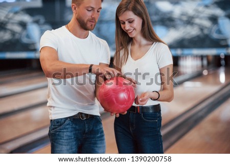 Hold it by that way. Man teaching girl how to holds ball and play bowling in the club.