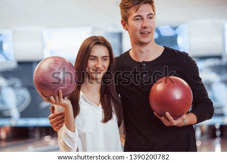 Happy couple holding bowling balls in hands and have good time in the club.