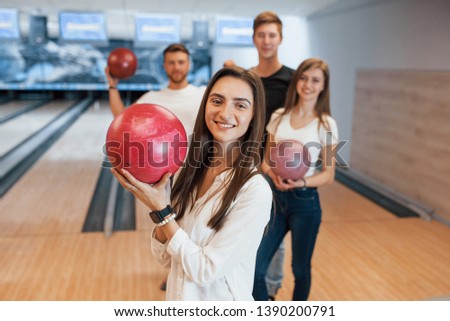 Brunette is happy to be there. Young cheerful friends have fun in bowling club at their weekends.