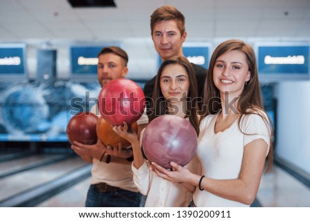 Holding balls in hands. Young cheerful friends have fun in bowling club at their weekends.