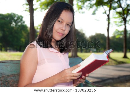 asian woman reading book in park.