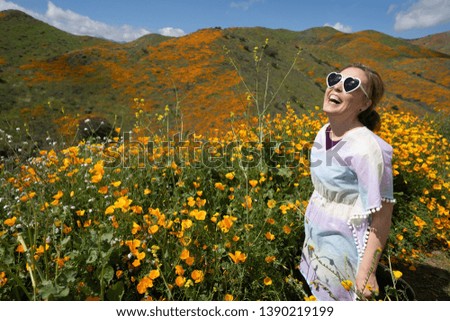 Young woman wearing heart sunglasses and casual clothing poses in poppy field