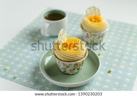 Tropical cupcakes decorated with piece of fresh mango and chocolate elements with a cup of green tea on green background