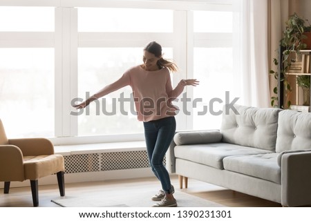 Full-length active young woman in casual clothes turn music on dancing moving in living room stands near window cozy modern interior sunny summer day, celebrating event, feels happy enjoy life concept Royalty-Free Stock Photo #1390231301