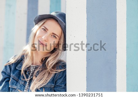 Happy pacified young woman in summer clothes sitting in urban space against a background of blue stripes on a warm summer day and enjoying the weekend. Copyspace