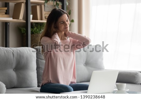 Frown woman sitting on couch near computer take break touches her neck suffers from painful feelings ache caused by poor wrong posture, sedentary work, sitting at laptop for long period concept image Royalty-Free Stock Photo #1390238648
