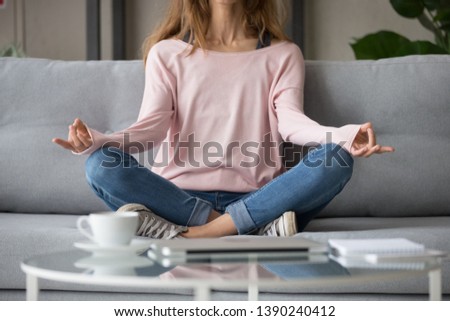 Cropped close up image woman in casual clothes sitting on sofa in lotus pose hands rests on laps, do yoga meditation practice breath exercise visualizes paint picture in mind no stress anxiety concept