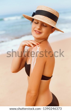 Woman Applying Sun Cream Creme on Tanned  Shoulder In Form Of The Sun. Sun Protection. Skin Care. Girl Using Sunscreen to Skin. Portrait Of Female Holding Suntan Lotion and Moisturizing Sunblock.