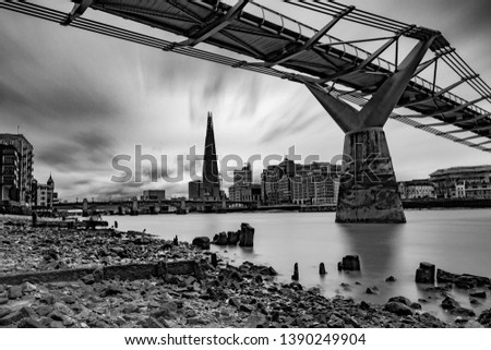A long exposure black and white image taken at low tide on the Thames, London, UK, showing the London skyline and one of the many bridges that span the river.