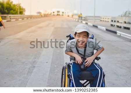 A child on wheelchair is smile happily, Amateur photographer hold camera in hand, Bridge  background and day light, Life in the education age of disabled children, Happy disabled kid concept.
