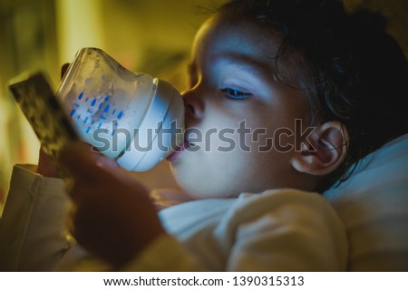 Two years old baby drinking milk and watching cartoons on phone
