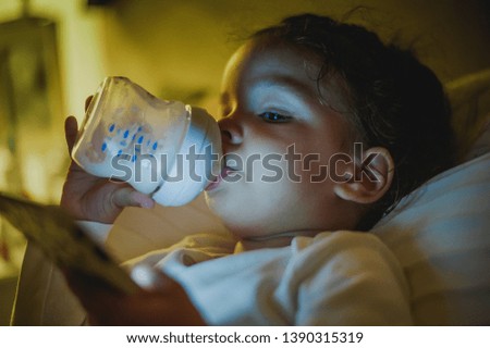 Two years old baby drinking milk and watching cartoons on phone