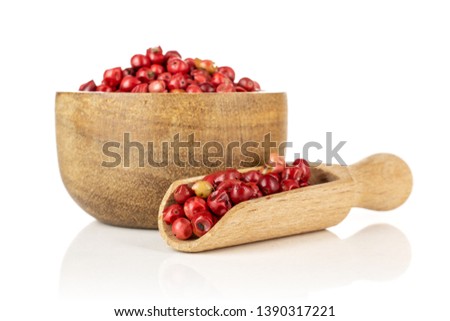 Lot of whole peruvian pink pepper in a wooden bowl with wooden scoop isolated on white background