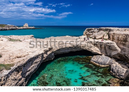 Archaeological site and tourist resort of Roca Vecchia, Puglia, Salento, Italy. Turquoise sea, clear blue sky, rocks, sun. The Cave of Poetry. Tourists sunbathe. The lookout tower in the background.