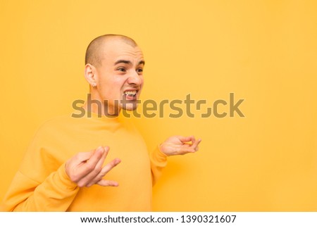 Authentic guy in yellow clothing makes funny, evil and looking away. Expressive crazy guy is isolated on a yellow background, makes a funny face. Copyspace