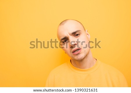 Stylish male rapper with grillz on his teeth poses on a yellow background wearing a yellow casual sweatshirt and balls. Portrait of a cool, authentic man, close and bright photo.