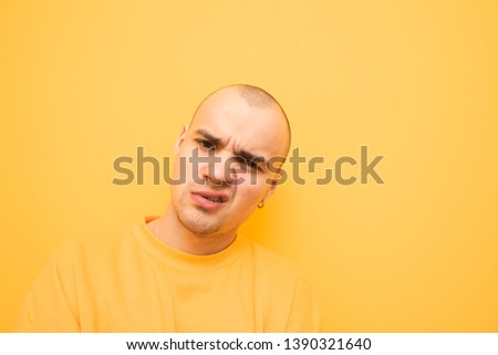 Portrait of a cool stylish guy in a yellow sweatshirt on a yellow background, looking into the camera and makes a serious face.Authentic rapper poses on the camera,studio photo on a yellow background