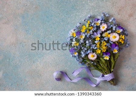 A bouquet of spring flowers of forget-me-nots, pansies and primroses on a colored background.