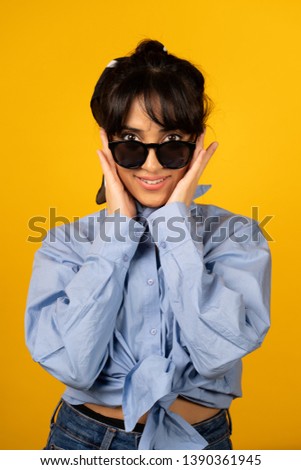 Young girl with in sunglasses posing for a photo on yellow background.
