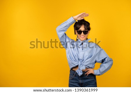 Young girl with in sunglasses posing for a photo on yellow background.